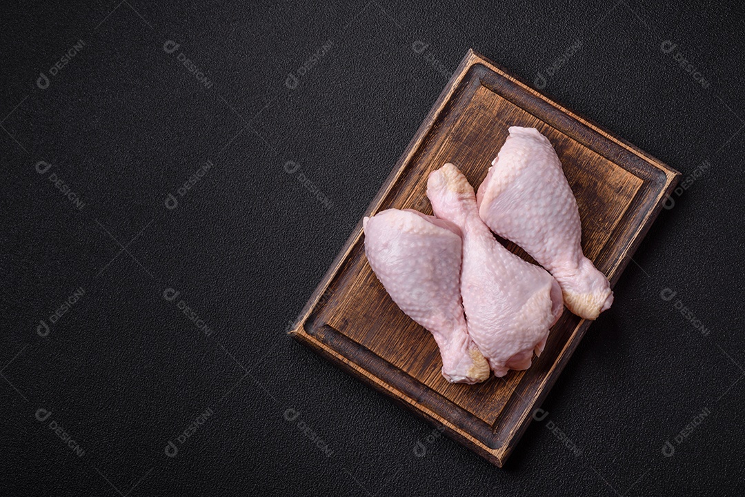 Pernas de frango cru com sal, especiarias e ervas sobre um fundo escuro de concreto preparado para assar