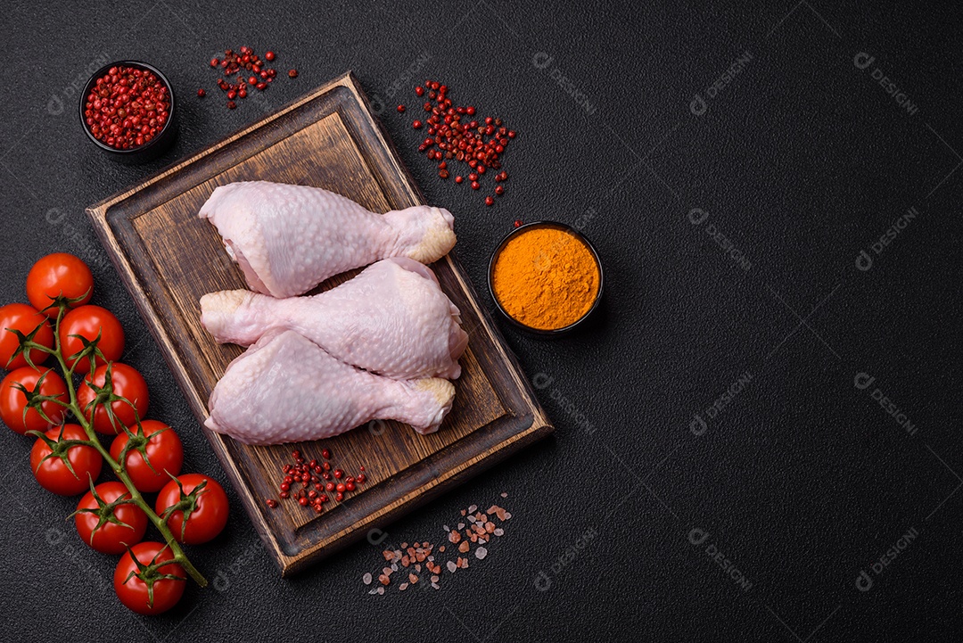Pernas de frango cru com sal, especiarias e ervas sobre um fundo escuro de concreto preparado para assar