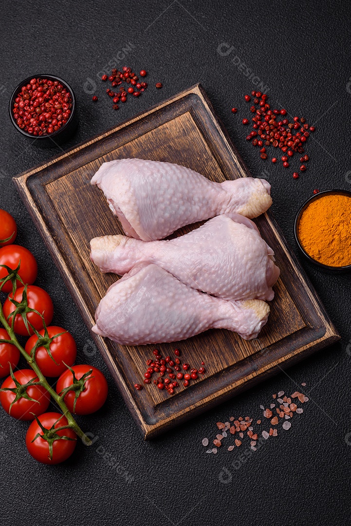 Pernas de frango cru com sal, especiarias e ervas sobre um fundo escuro de concreto preparado para assar