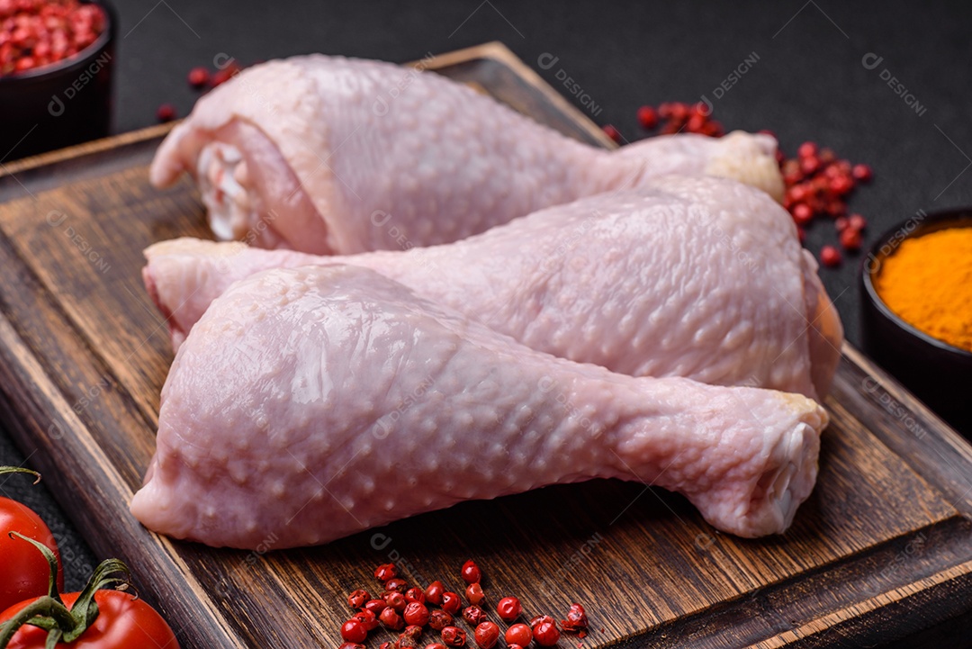 Pernas de frango cru com sal, especiarias e ervas sobre um fundo escuro de concreto preparado para assar