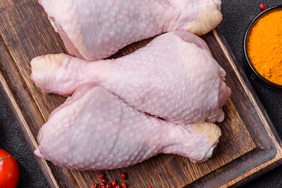 Pernas de frango cru com sal, especiarias e ervas sobre um fundo escuro de concreto preparado para assar