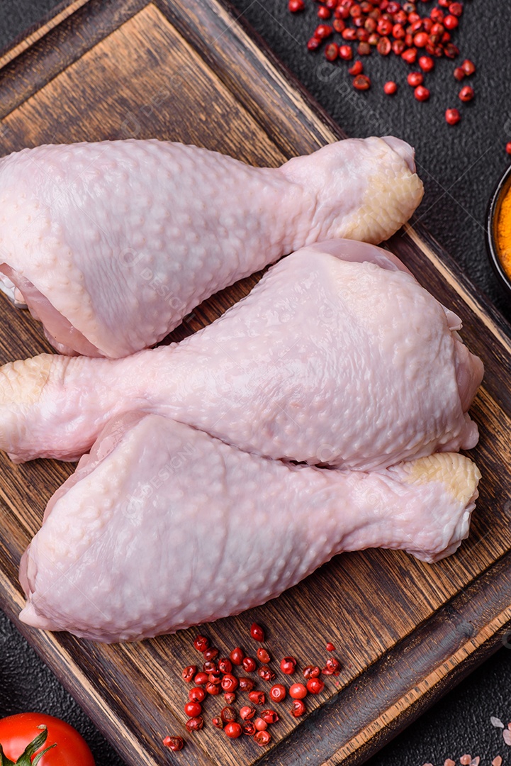 Pernas de frango cru com sal, especiarias e ervas sobre um fundo escuro de concreto preparado para assar