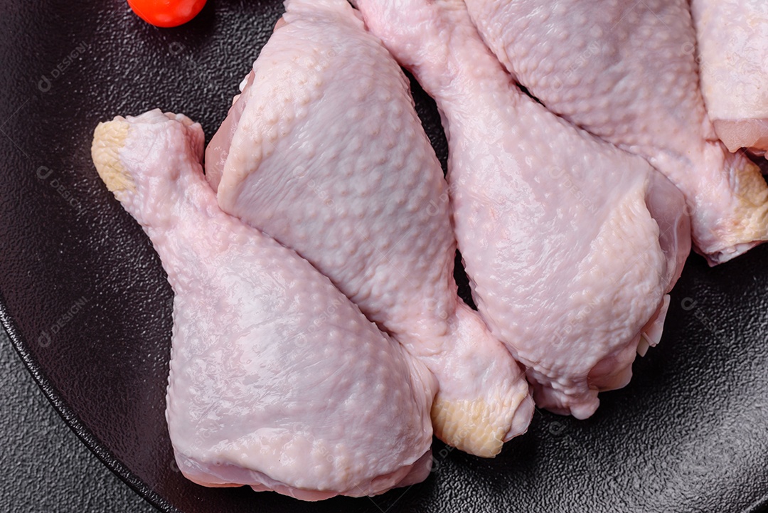 Pernas de frango cru com sal, especiarias e ervas sobre um fundo escuro de concreto preparado para assar