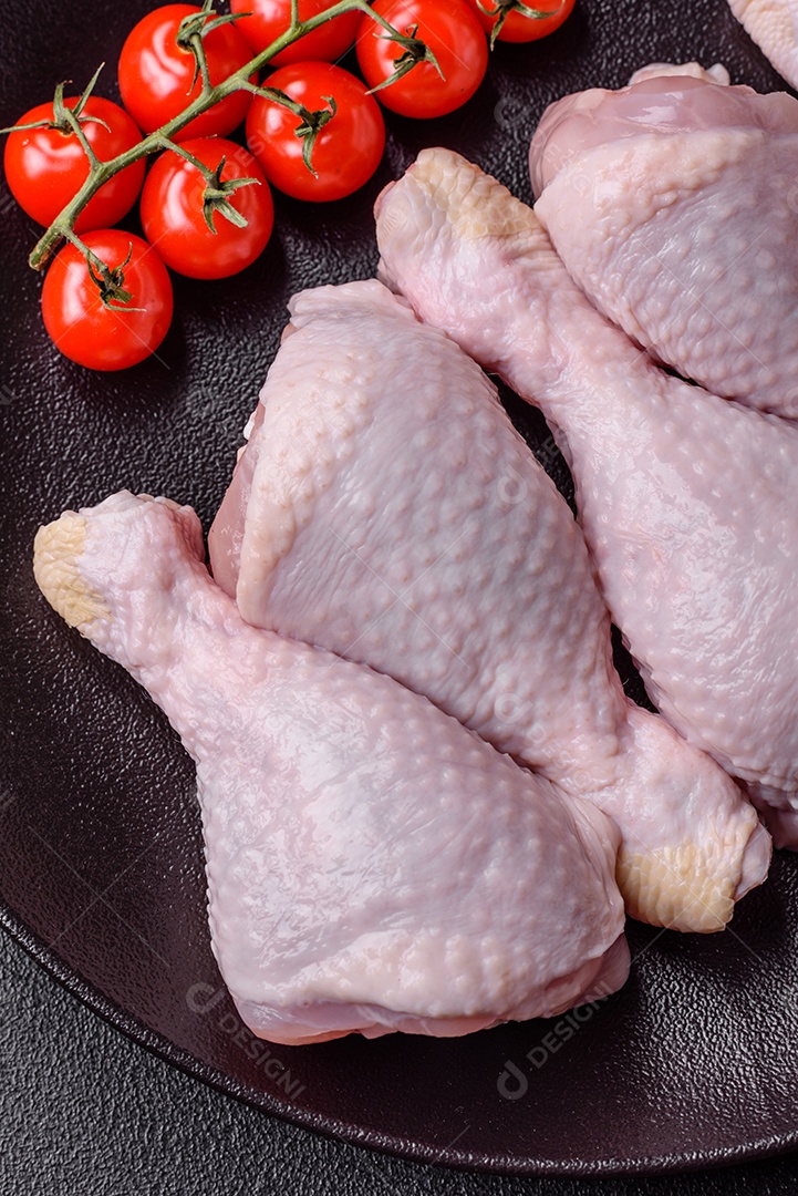 Pernas de frango cru com sal, especiarias e ervas sobre um fundo escuro de concreto preparado para assar