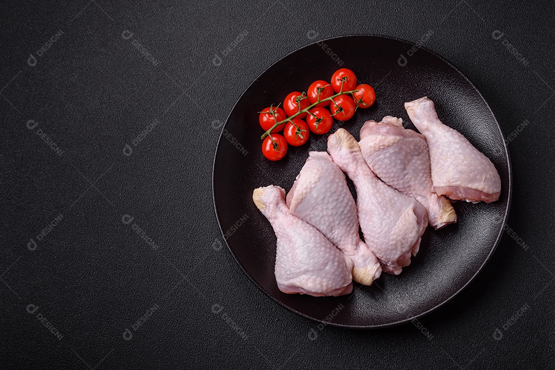 Pernas de frango cru com sal, especiarias e ervas sobre um fundo escuro de concreto preparado para assar