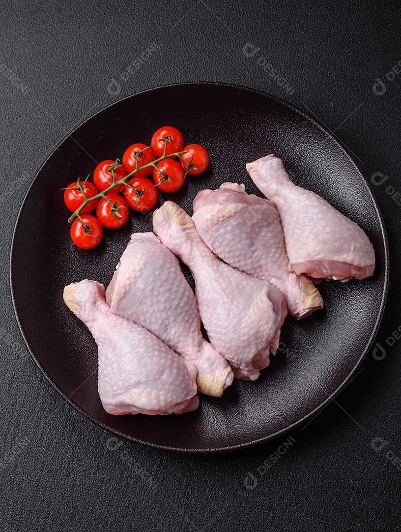 Pernas de frango cru com sal, especiarias e ervas sobre um fundo escuro de concreto preparado para assar