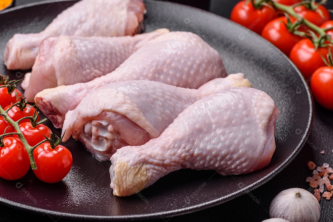 Pernas de frango cru com sal, especiarias e ervas sobre um fundo escuro de concreto preparado para assar