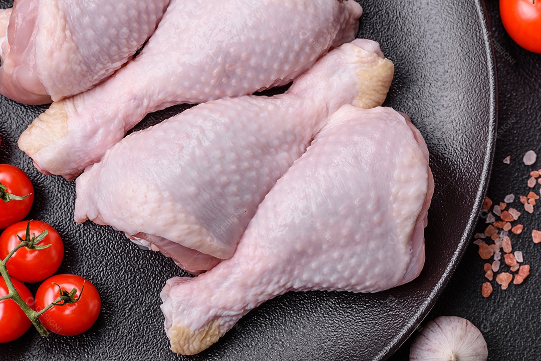 Pernas de frango cru com sal, especiarias e ervas sobre um fundo escuro de concreto preparado para assar