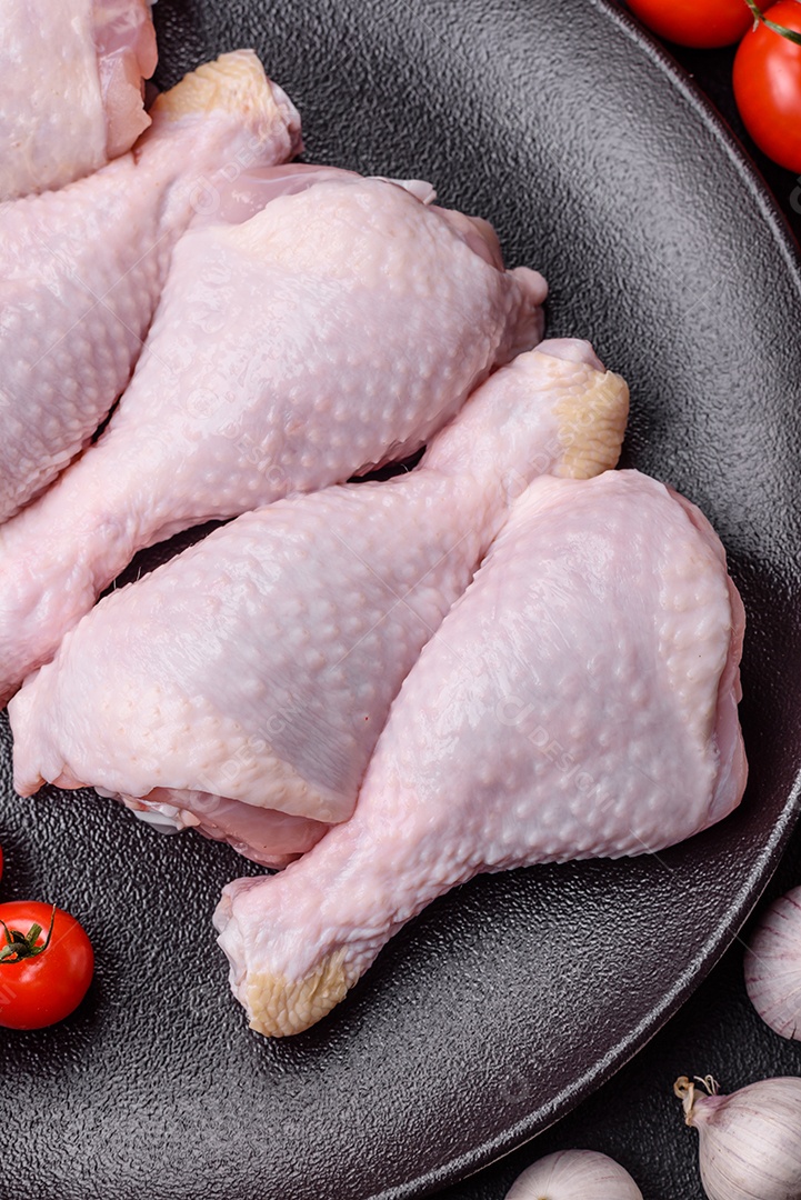 Pernas de frango cru com sal, especiarias e ervas sobre um fundo escuro de concreto preparado para assar