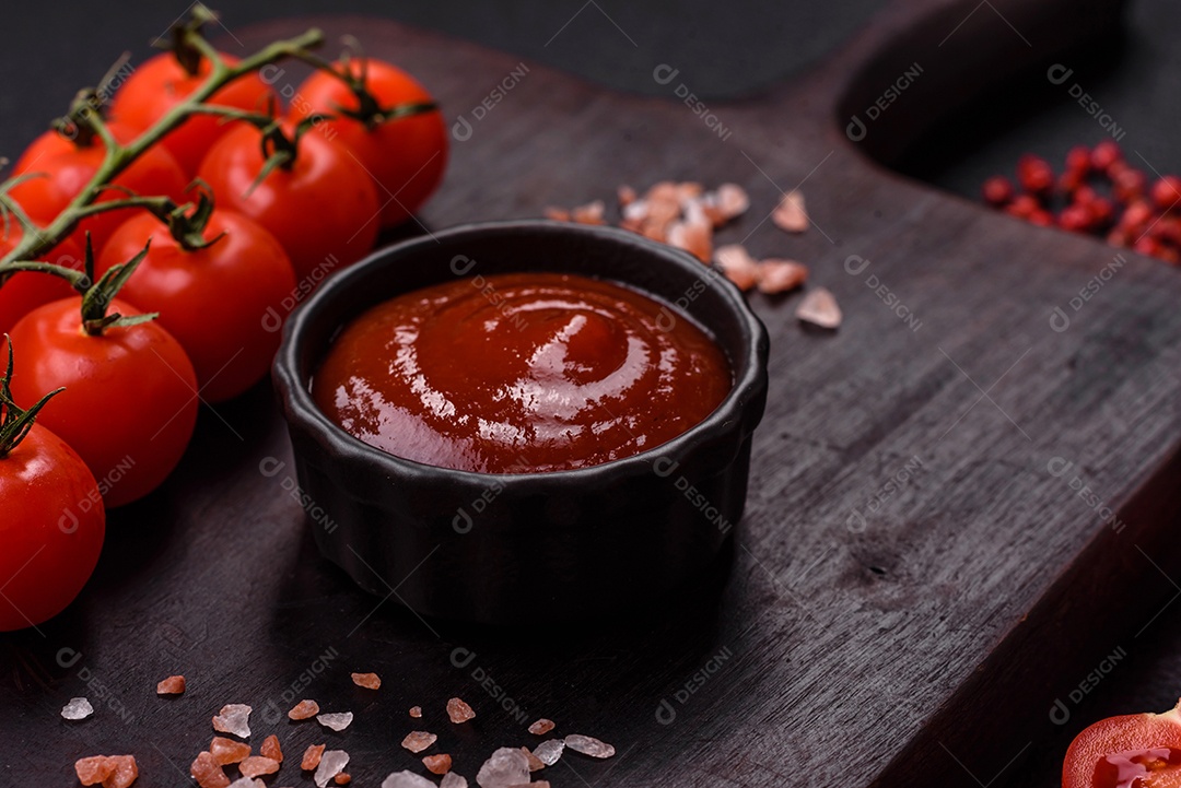 Delicioso molho de tomate picante com pimenta, alho, sal, especiarias e ervas em uma molheira branca sobre um fundo escuro de concreto