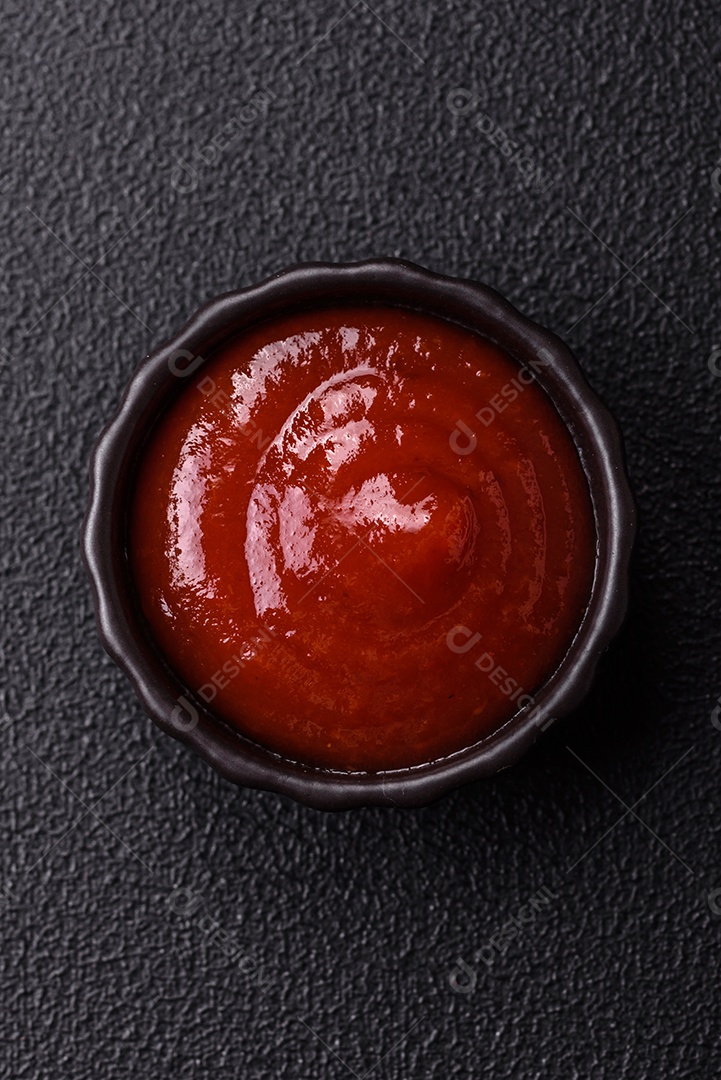 Delicioso molho de tomate picante com pimenta, alho, sal, especiarias e ervas em uma molheira branca sobre um fundo escuro de concreto