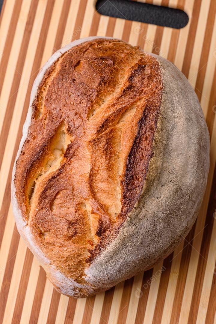 Um pedaço de pão integral com grãos de cereais em uma tábua de madeira sobre um fundo escuro de concreto