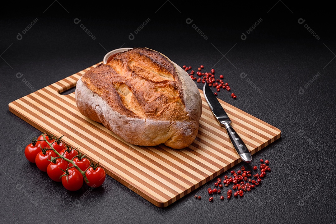 Um pedaço de pão integral com grãos de cereais em uma tábua de madeira sobre um fundo escuro de concret