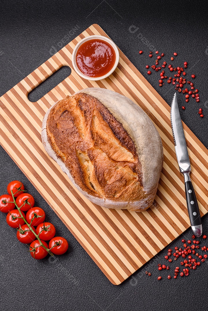 Um pedaço de pão integral com grãos de cereais em uma tábua de madeira sobre um fundo escuro de concreto