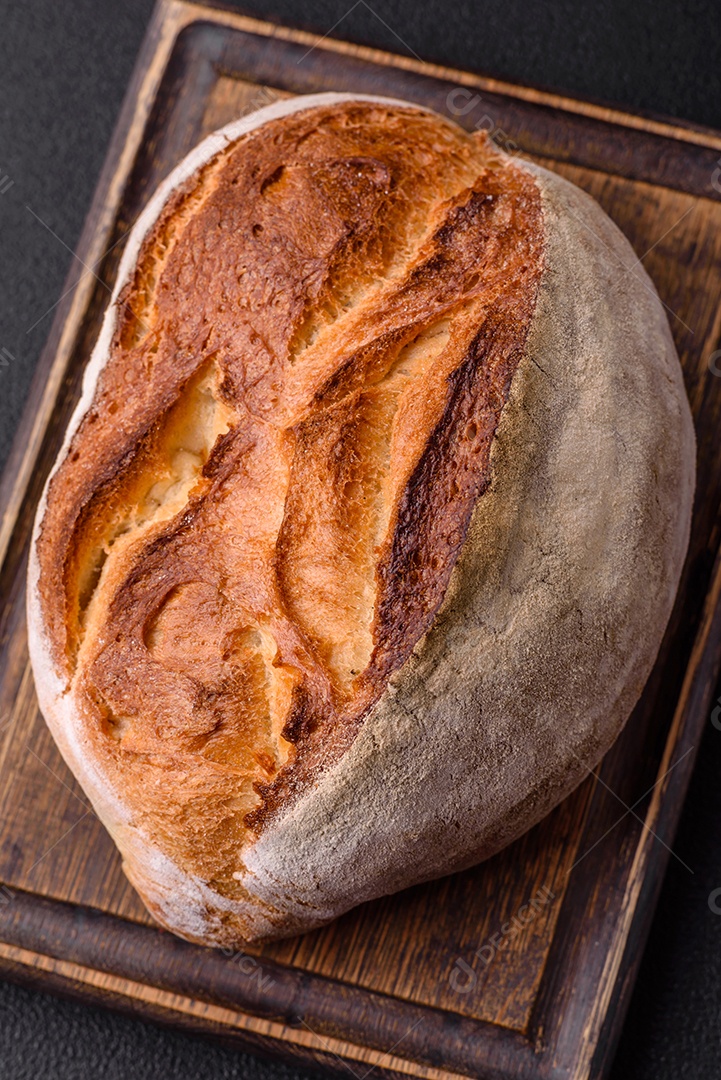 Um pedaço de pão integral com grãos de cereais em uma tábua de madeira sobre um fundo escuro de concreto