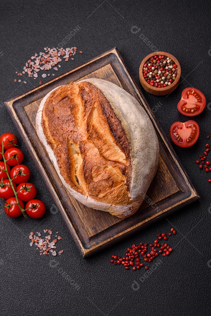 Um pedaço de pão integral com grãos de cereais em uma tábua de madeira sobre um fundo escuro de concreto