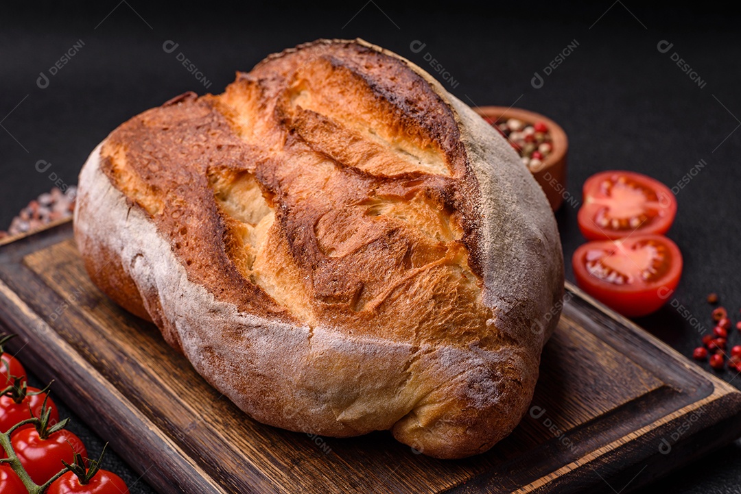 Um pedaço de pão integral com grãos de cereais em uma tábua de madeira sobre um fundo escuro de concreto