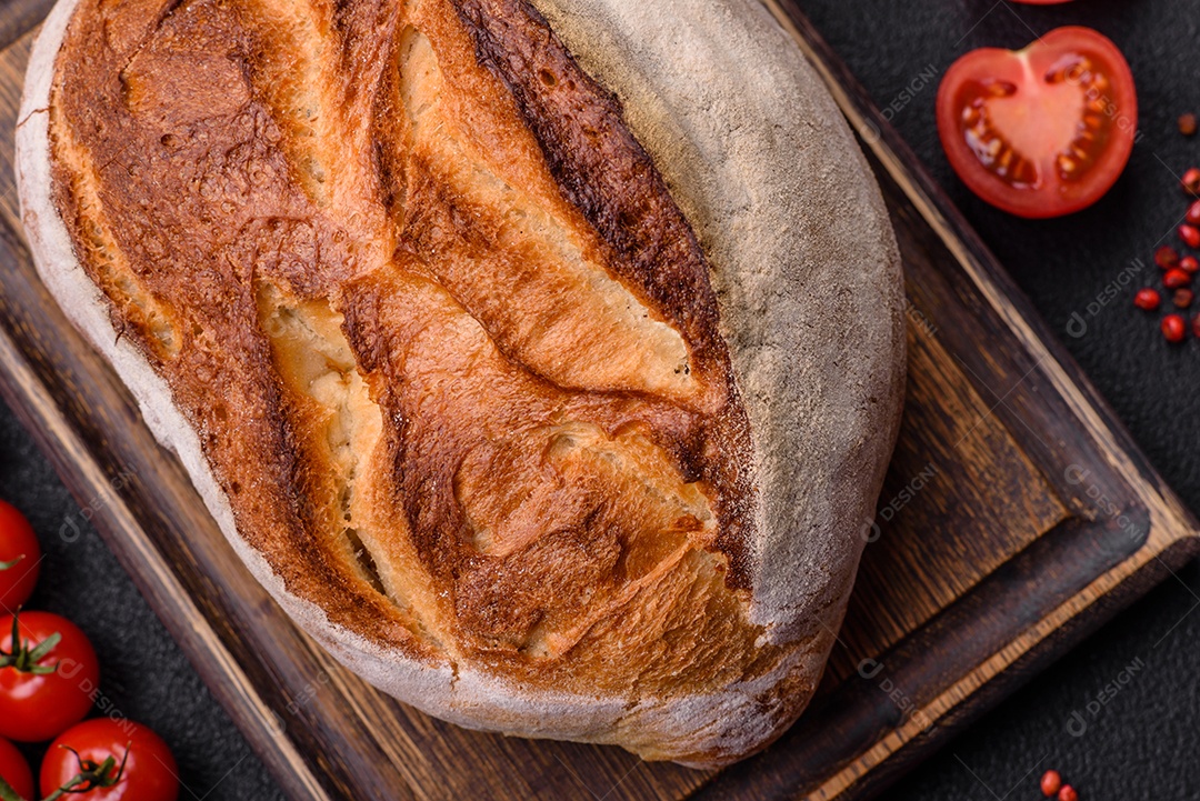 Um pedaço de pão integral com grãos de cereais em uma tábua de madeira sobre um fundo escuro de concreto