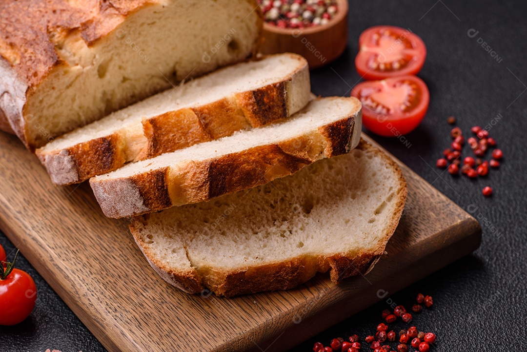 Um pedaço de pão integral com grãos de cereais em uma tábua de madeira sobre um fundo escuro de concreto