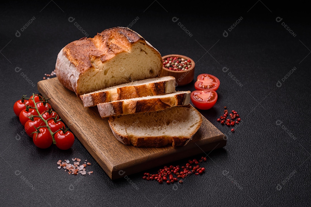 Um pedaço de pão integral com grãos de cereais em uma tábua de madeira sobre um fundo escuro de concreto