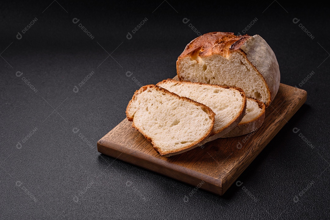 Um pedaço de pão integral com grãos de cereais em uma tábua de madeira sobre um fundo escuro de concreto