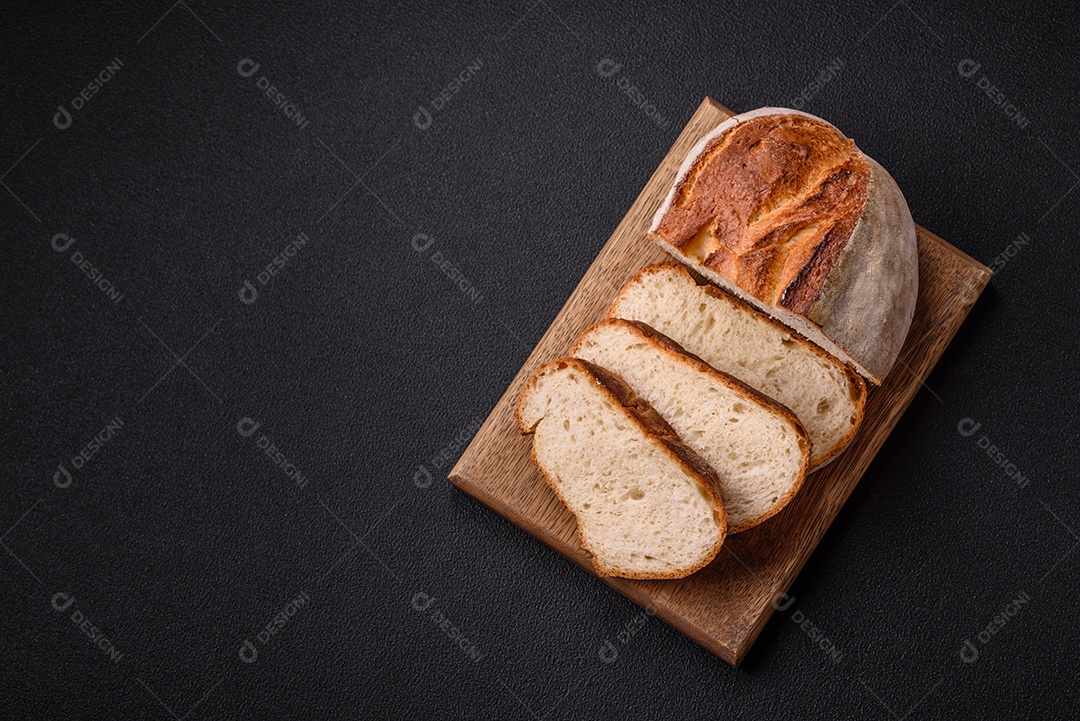 Um pedaço de pão integral com grãos de cereais em uma tábua de madeira sobre um fundo escuro de concreto