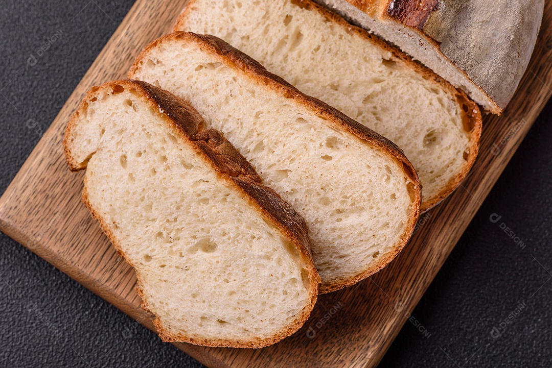 Um pedaço de pão integral com grãos de cereais em uma tábua de madeira sobre um fundo escuro de concreto