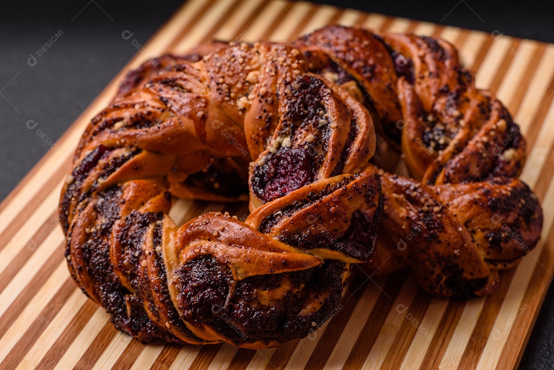 Delicioso pão fresco com sementes de papoila e bagas em forma de anel sobre um fundo escuro de concreto