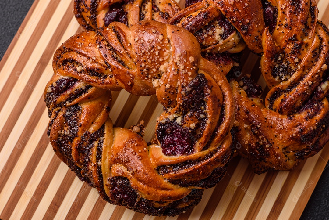Delicioso pão fresco com sementes de papoila e bagas em forma de anel sobre um fundo escuro de concreto