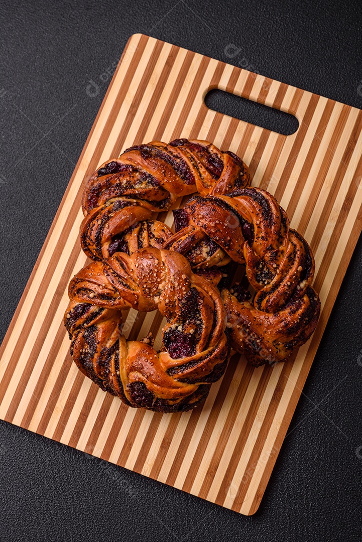 Delicioso pão fresco com sementes de papoila e bagas em forma de anel sobre um fundo escuro de concreto