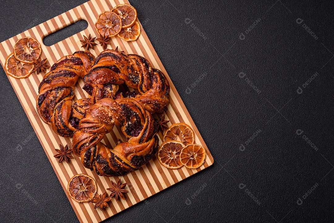 Delicioso pão fresco com sementes de papoila e bagas em forma de anel sobre um fundo escuro de concreto