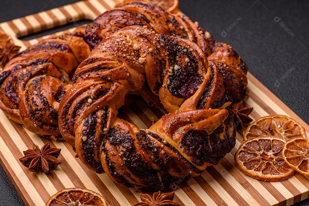 Delicioso pão fresco com sementes de papoila e bagas em forma de anel sobre um fundo escuro de concreto