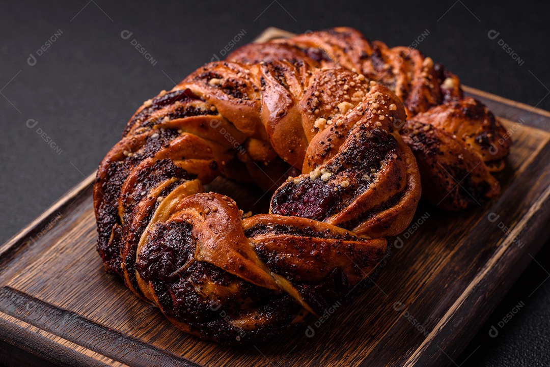 Delicioso pão fresco com sementes de papoila e bagas em forma de anel sobre um fundo escuro de concreto