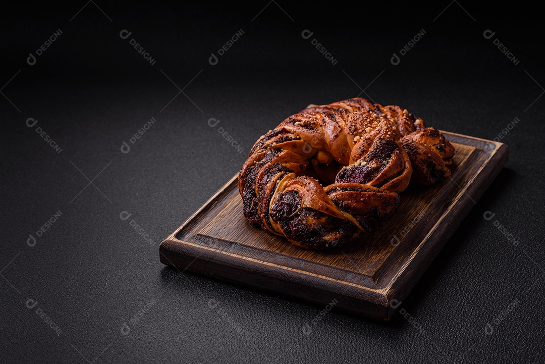 Delicioso pão fresco com sementes de papoila e bagas em forma de anel sobre um fundo escuro de concreto