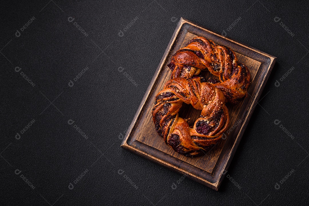 Delicioso pão fresco com sementes de papoila e bagas em forma de anel sobre um fundo escuro de concreto