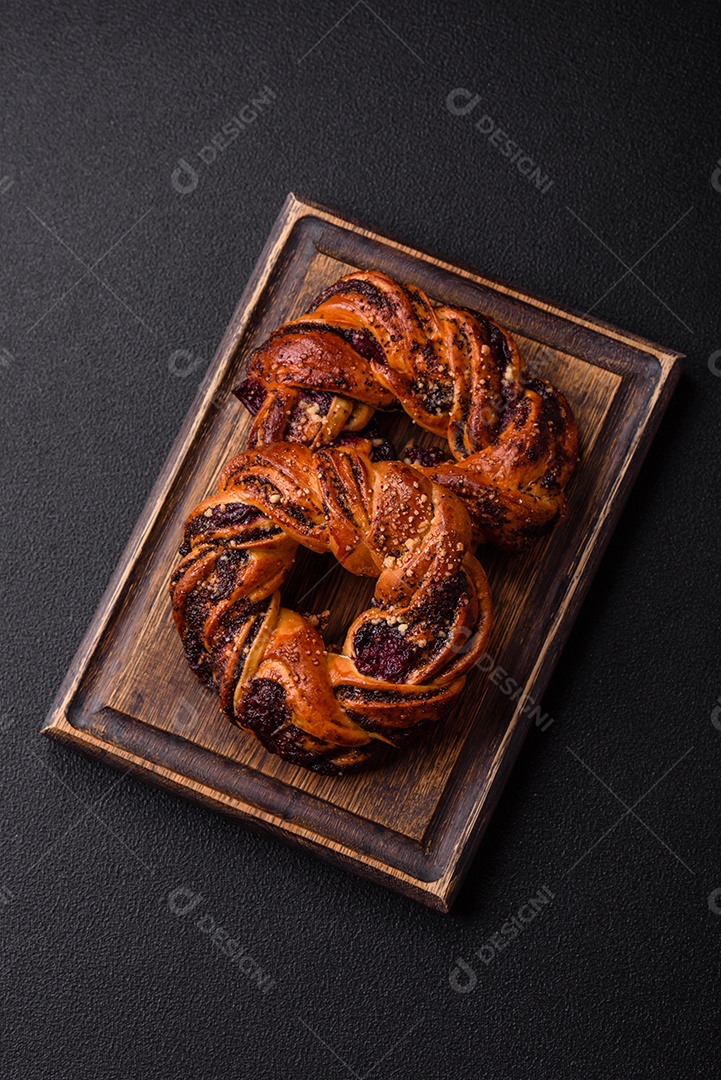 Delicioso pão fresco com sementes de papoila e bagas em forma de anel sobre um fundo escuro de concreto