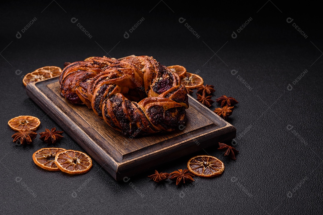 Delicioso pão fresco com sementes de papoila e bagas em forma de anel sobre um fundo escuro de concreto