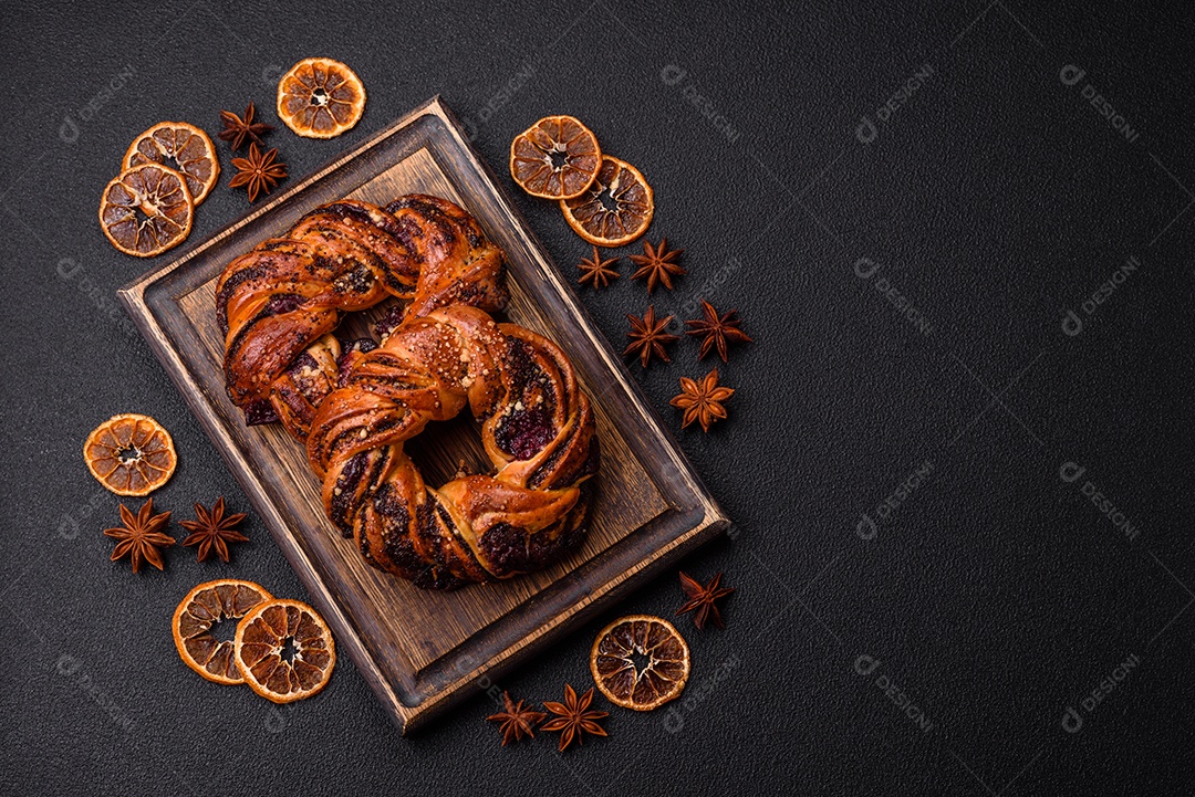 Delicioso pão fresco com sementes de papoila e bagas em forma de anel sobre um fundo escuro de concreto