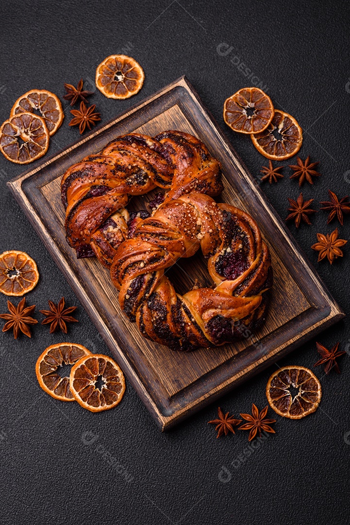 Delicioso pão fresco com sementes de papoila e bagas em forma de anel sobre um fundo escuro de concreto