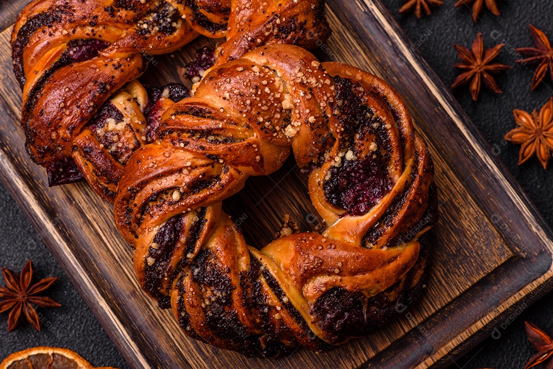 Delicioso pão fresco com sementes de papoila e bagas em forma de anel sobre um fundo escuro de concreto