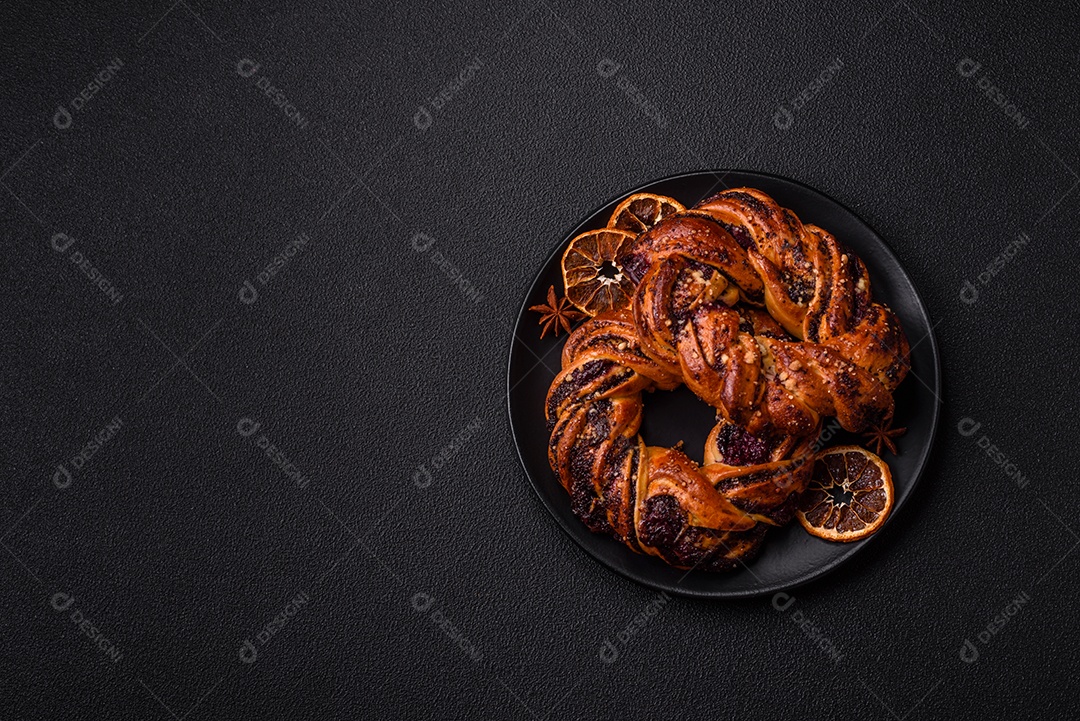 Delicioso pão fresco com sementes de papoila e bagas em forma de anel sobre um fundo escuro de concreto