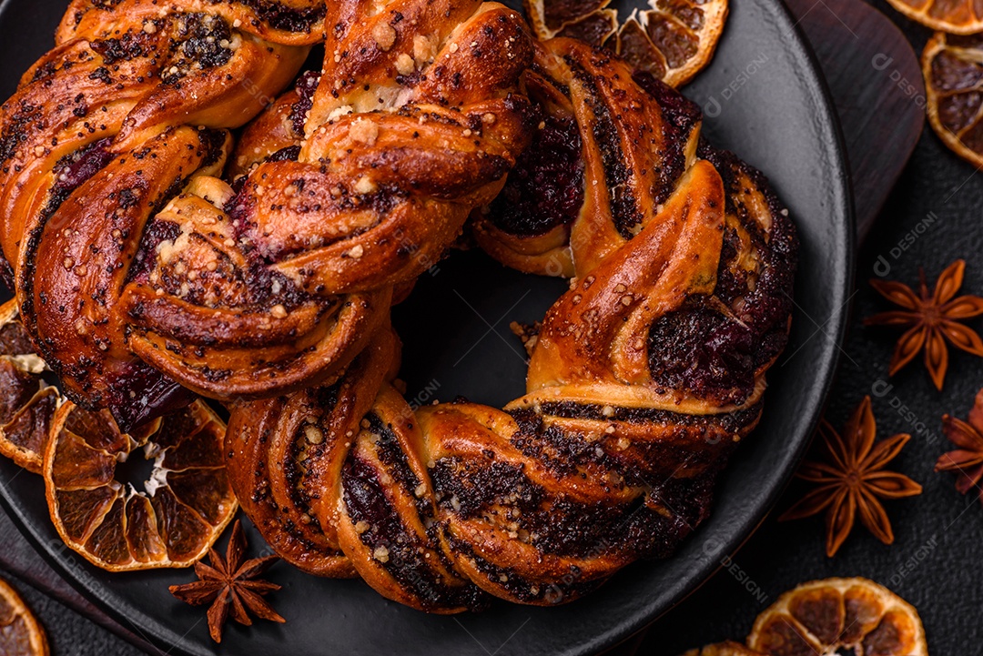 Delicioso pão fresco com sementes de papoila e bagas em forma de anel sobre um fundo escuro de concreto