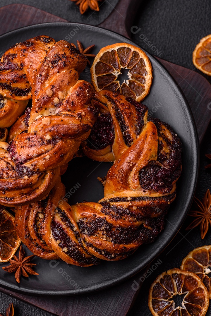 Delicioso pão fresco com sementes de papoila e bagas em forma de anel sobre um fundo escuro de concreto
