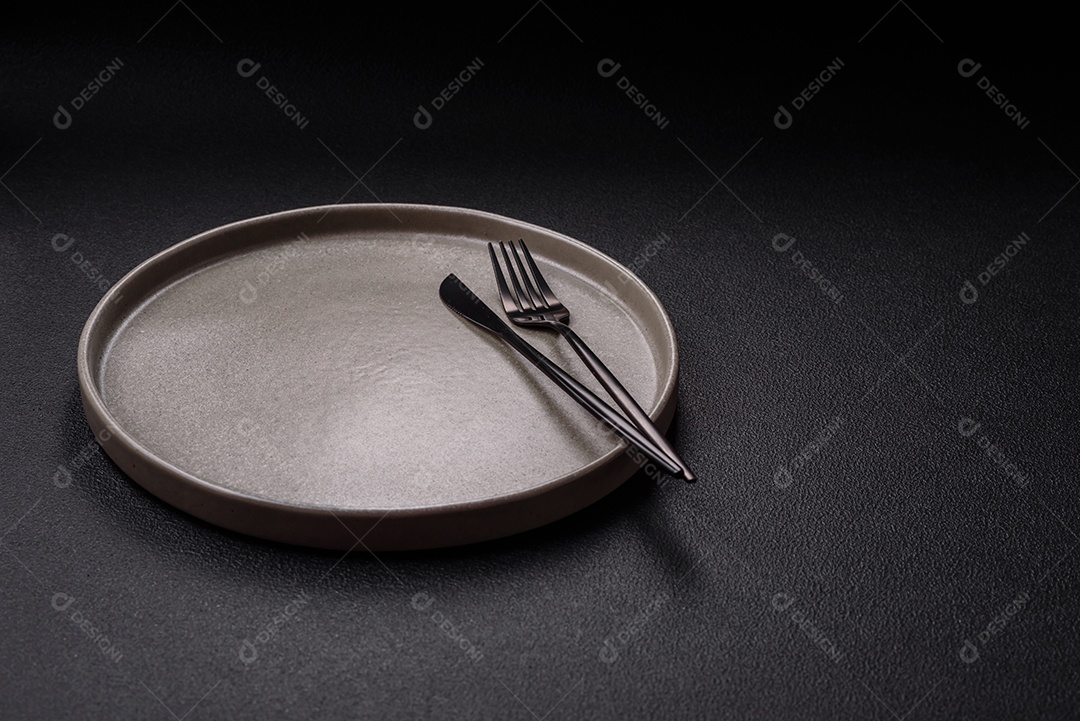 Placa redonda de cerâmica vazia em fundo de concreto texturizado escuro. Talheres, preparação para o jantar