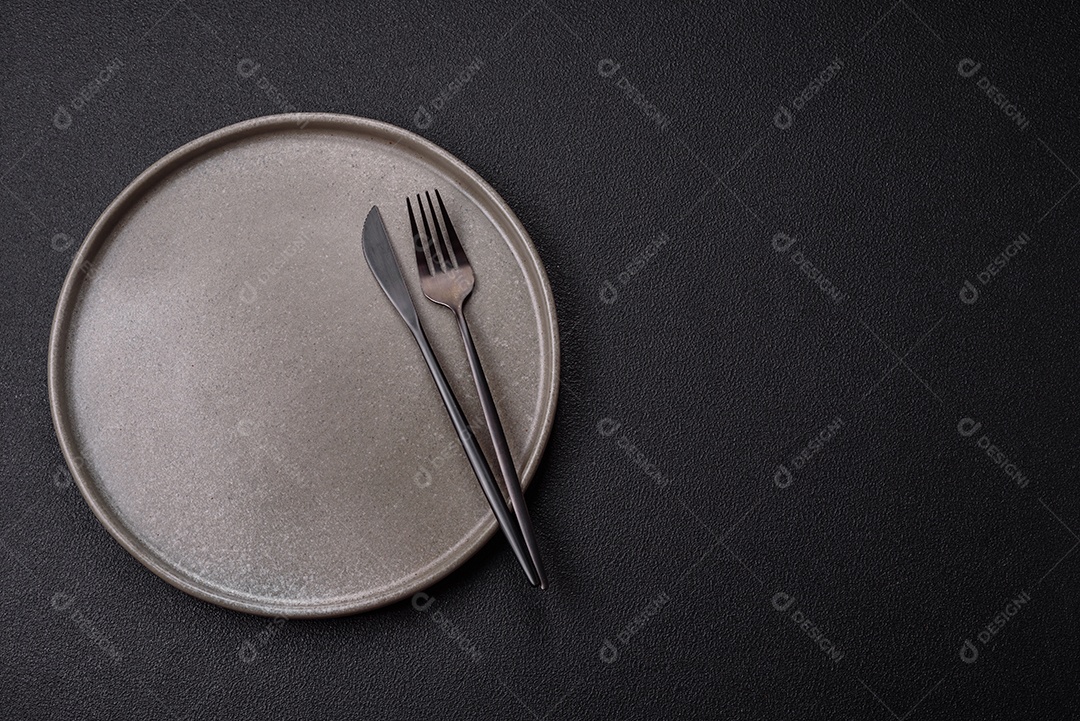 Placa redonda de cerâmica vazia em fundo de concreto texturizado escuro. Talheres, preparação para o jantar