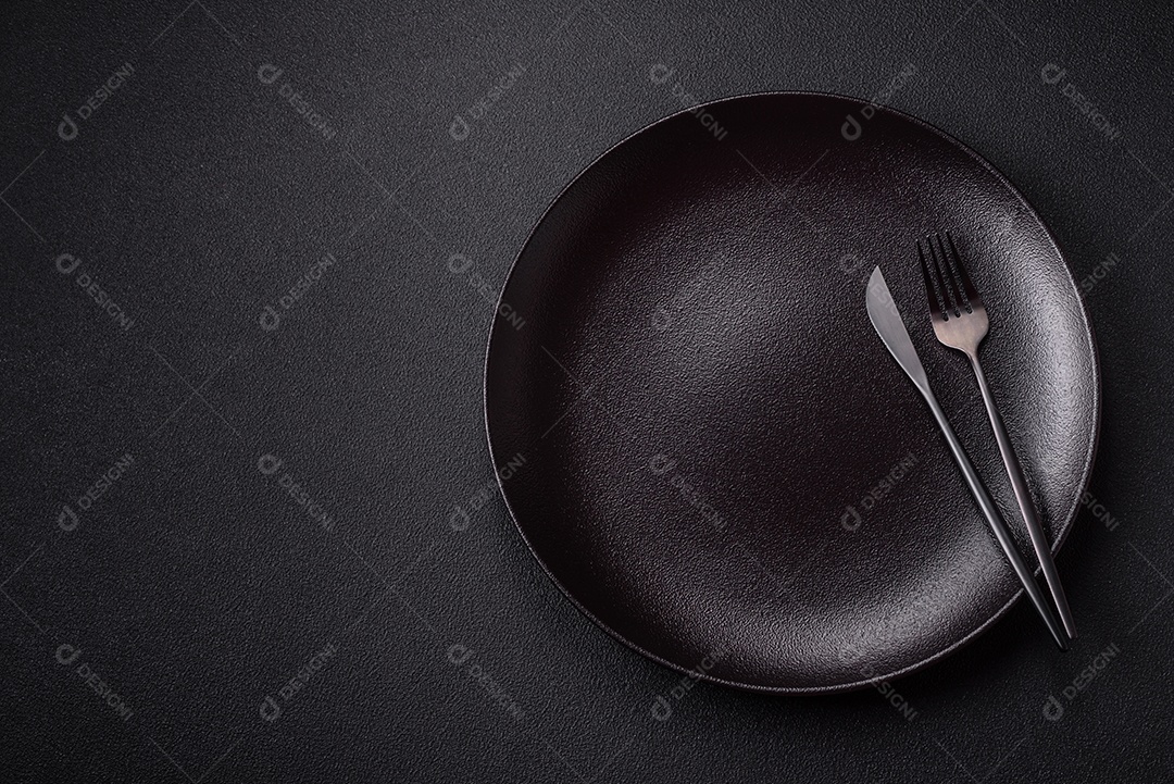 Placa redonda de cerâmica vazia em fundo de concreto texturizado escuro. Talheres, preparação para o jantar