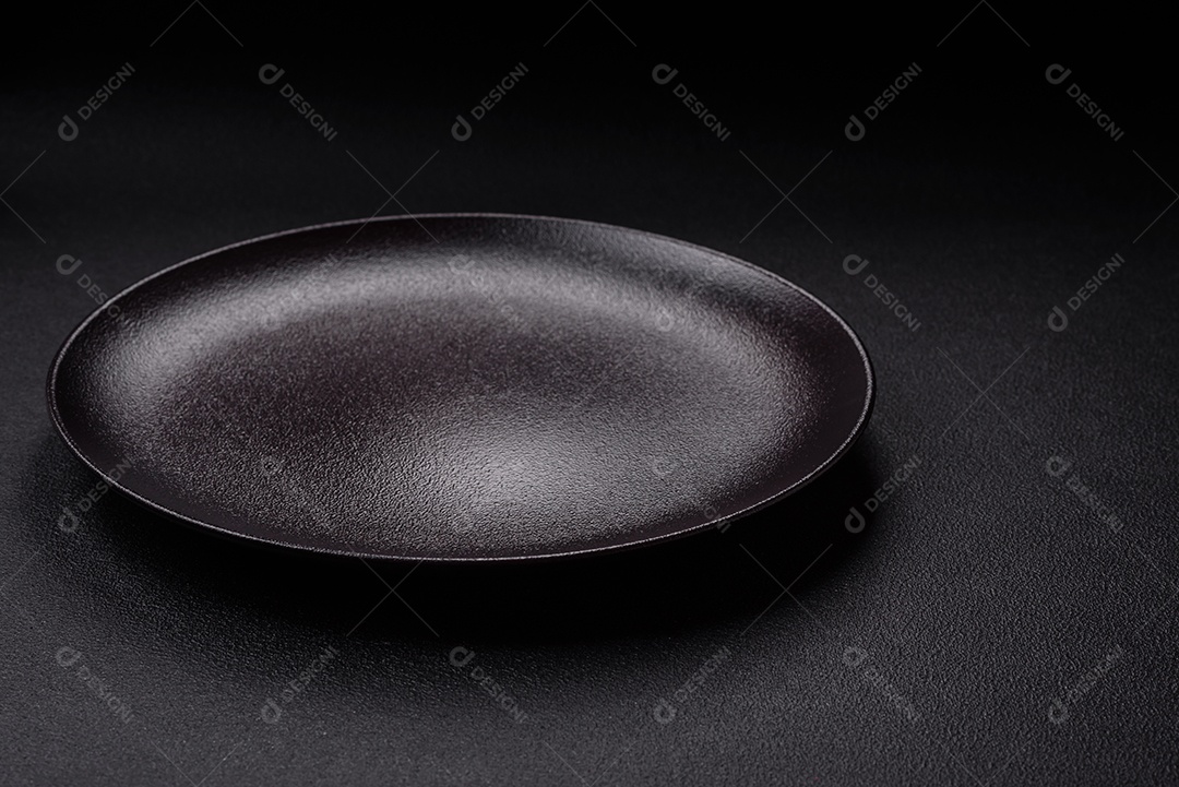 Placa redonda de cerâmica vazia em fundo de concreto texturizado escuro. Talheres, preparação para o jantar