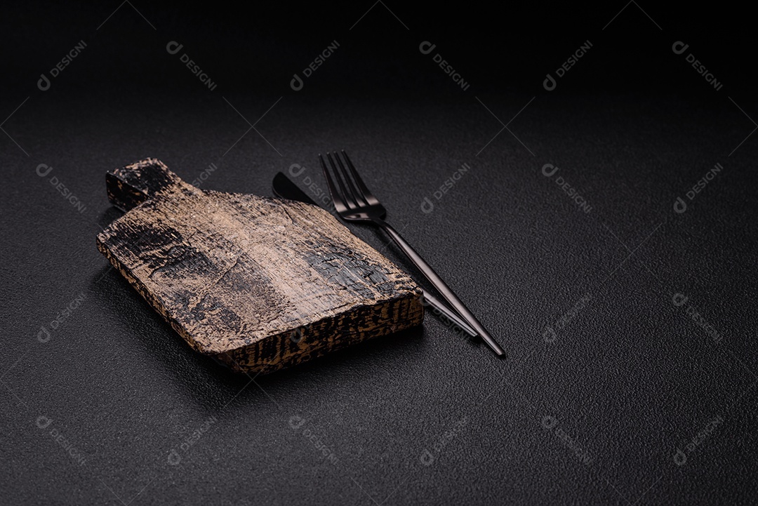 Tábua de corte de madeira vazia em fundo de concreto texturizado escuro. Talheres, preparação para o jantar