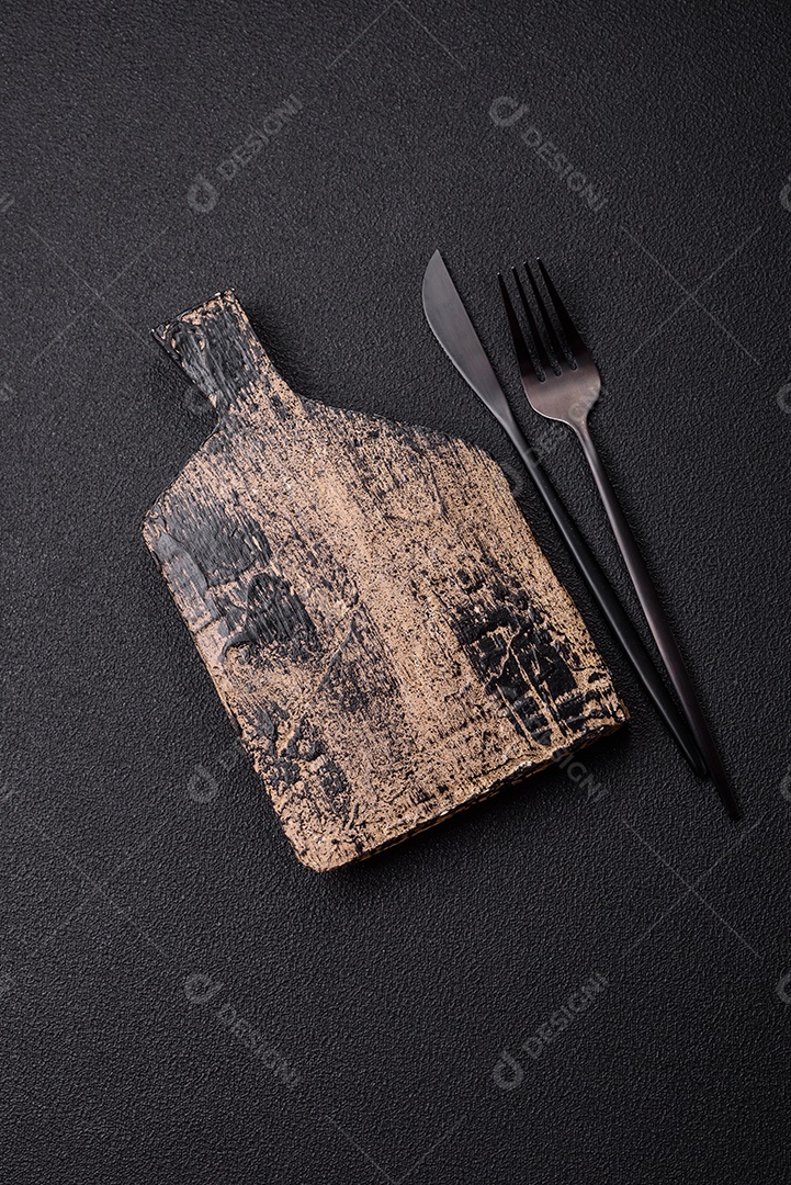 Tábua de corte de madeira vazia em fundo de concreto texturizado escuro. Talheres, preparação para o jantar