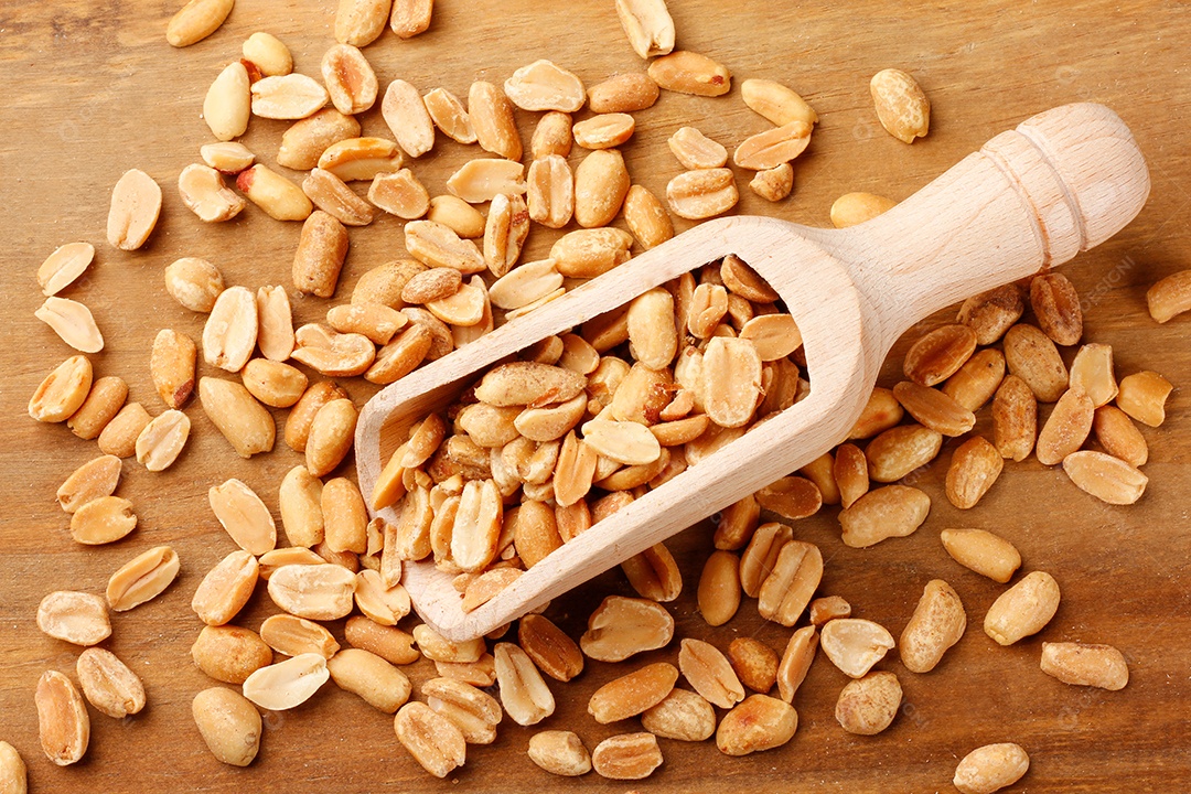 Amendoim torrado descascado em colher de pau isolado em fundo branco